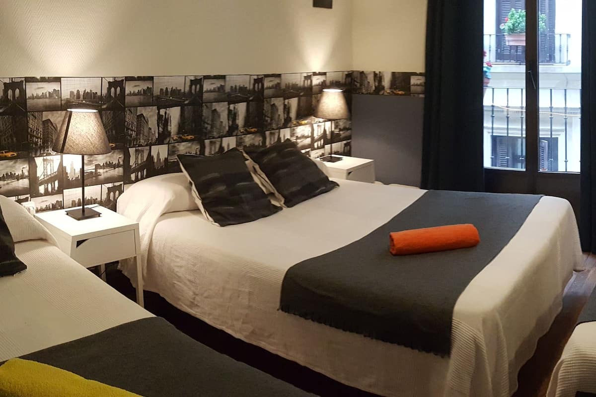 A hotel room with two beds, a nightstand, a lamp, and a view of the city through the window.