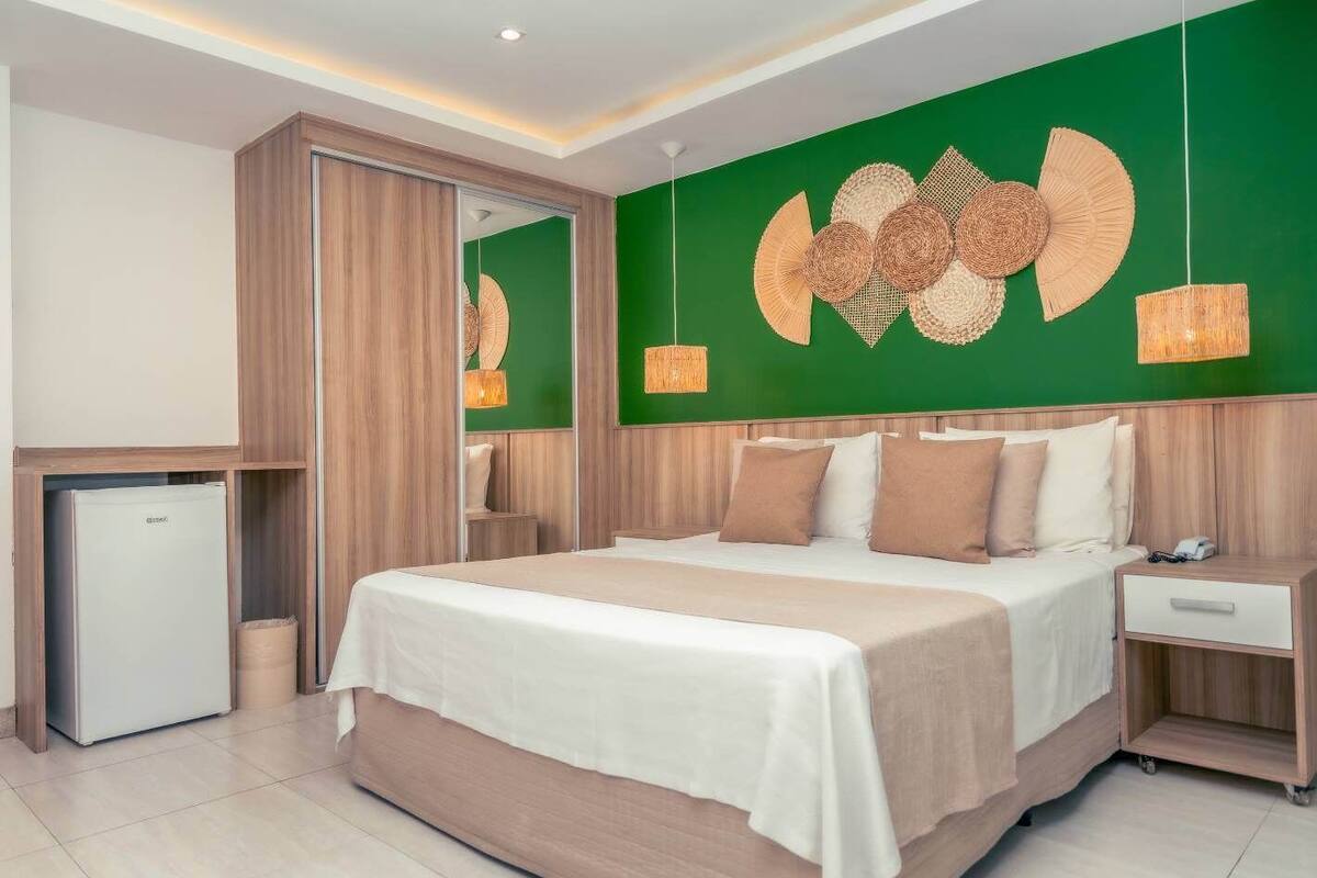 A modern hotel room with a large bed, a small refrigerator, and a green accent wall with decorative wall art.