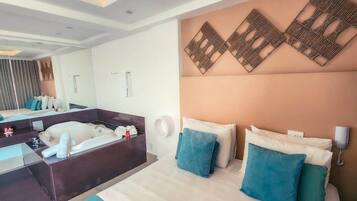 Quarto de hotel moderno com uma cama grande, banheiro separado, uma pequena escrivaninha e um detalhe decorativo na parede.