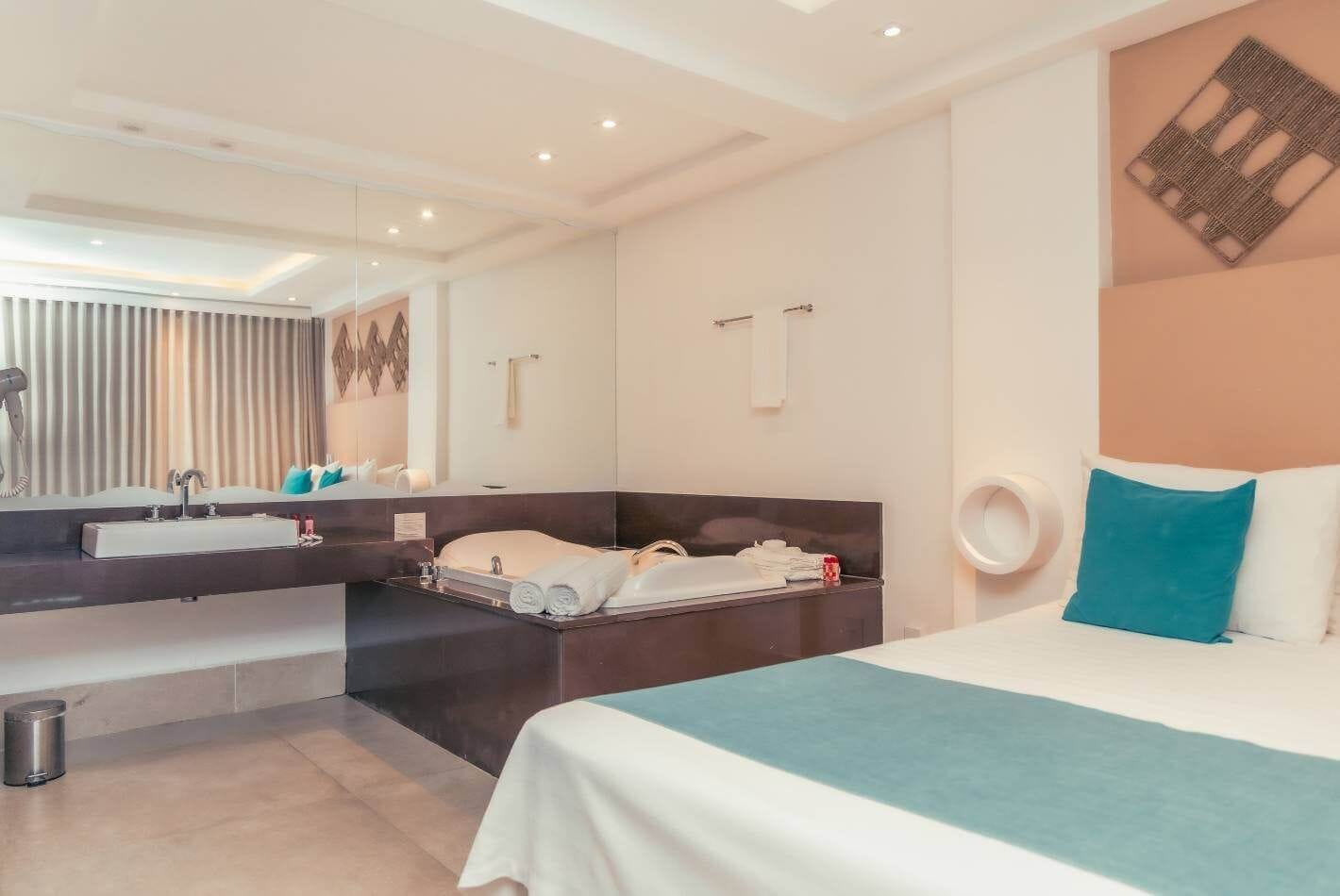 A modern hotel room with a large bed, a separate bathroom area, a vanity with a mirror, and a small trash bin.