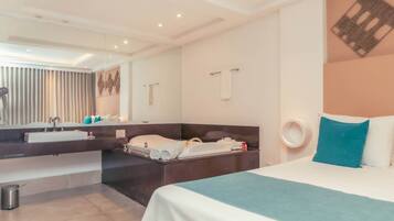 A modern hotel room with a large bed, a separate bathroom area, a vanity with a mirror, and a small trash bin.