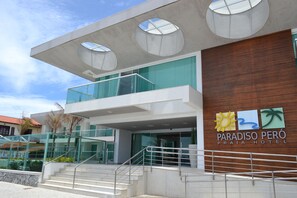 A modern hotel with a glass facade, a wooden panel wall, and a sign for Paradiso Peró Praia Hotel. - Paradiso Pero Praia Hotel (Cabo Frio)