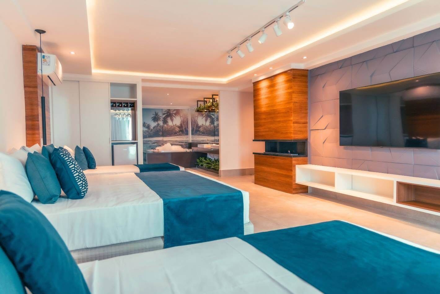 A modern bedroom with a large bed, a TV, and a small kitchenette.