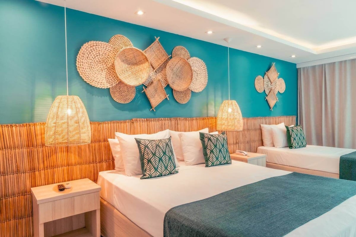 Une chambre d’hôtel avec un grand lit, deux tables de chevet, un mur orné d’une décoration murale tissée et un luminaire suspendu.