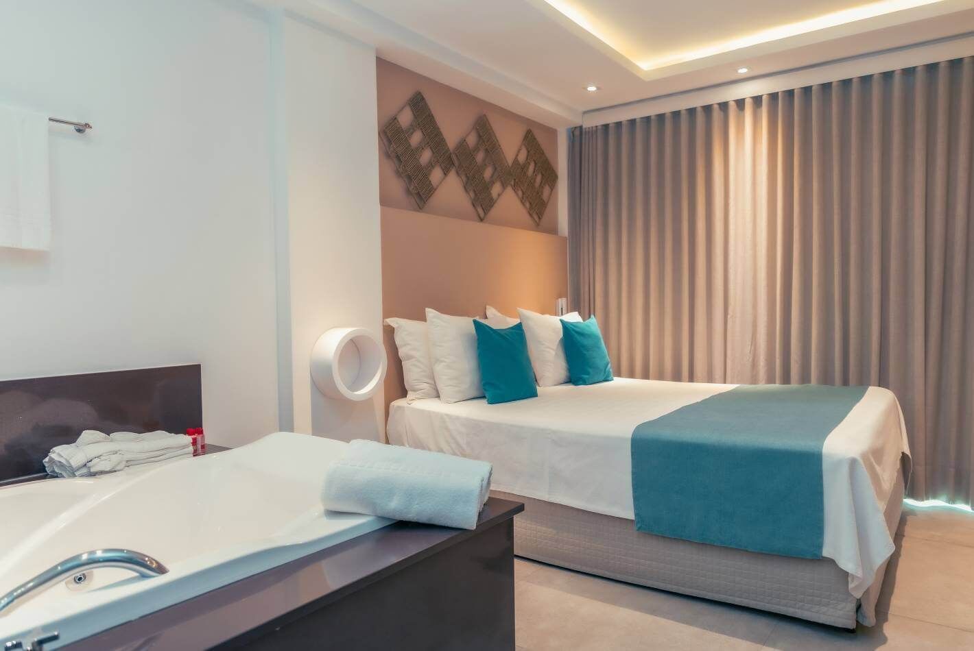 Una habitación de hotel con cama, mesita de noche, espejo y lámpara de pared.