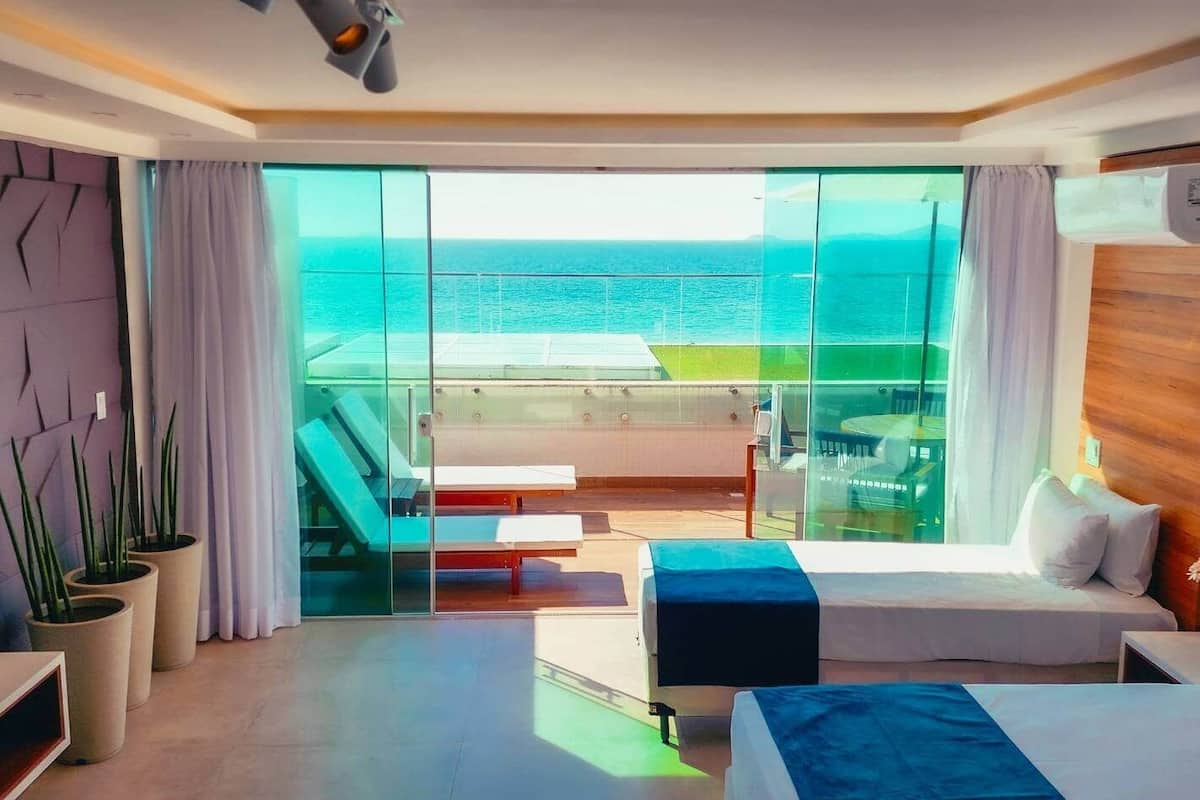 Une chambre d’hôtel moderne dotée d’une grande porte-fenêtre coulissante donnant sur un balcon avec vue sur l’océan.