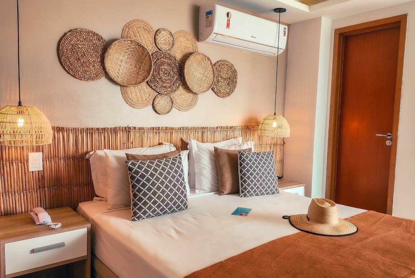 A hotel room with a bed, bedside tables, a wall-mounted air conditioner, and a woven wall decoration.