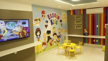 Uma sala de jogos infantil com televisão, decorações coloridas nas paredes e móveis amarelos.