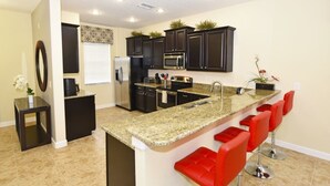 A modern kitchen with dark cabinets, granite countertops, and red bar stools. - Providence 2323EVDIL (Davenport)