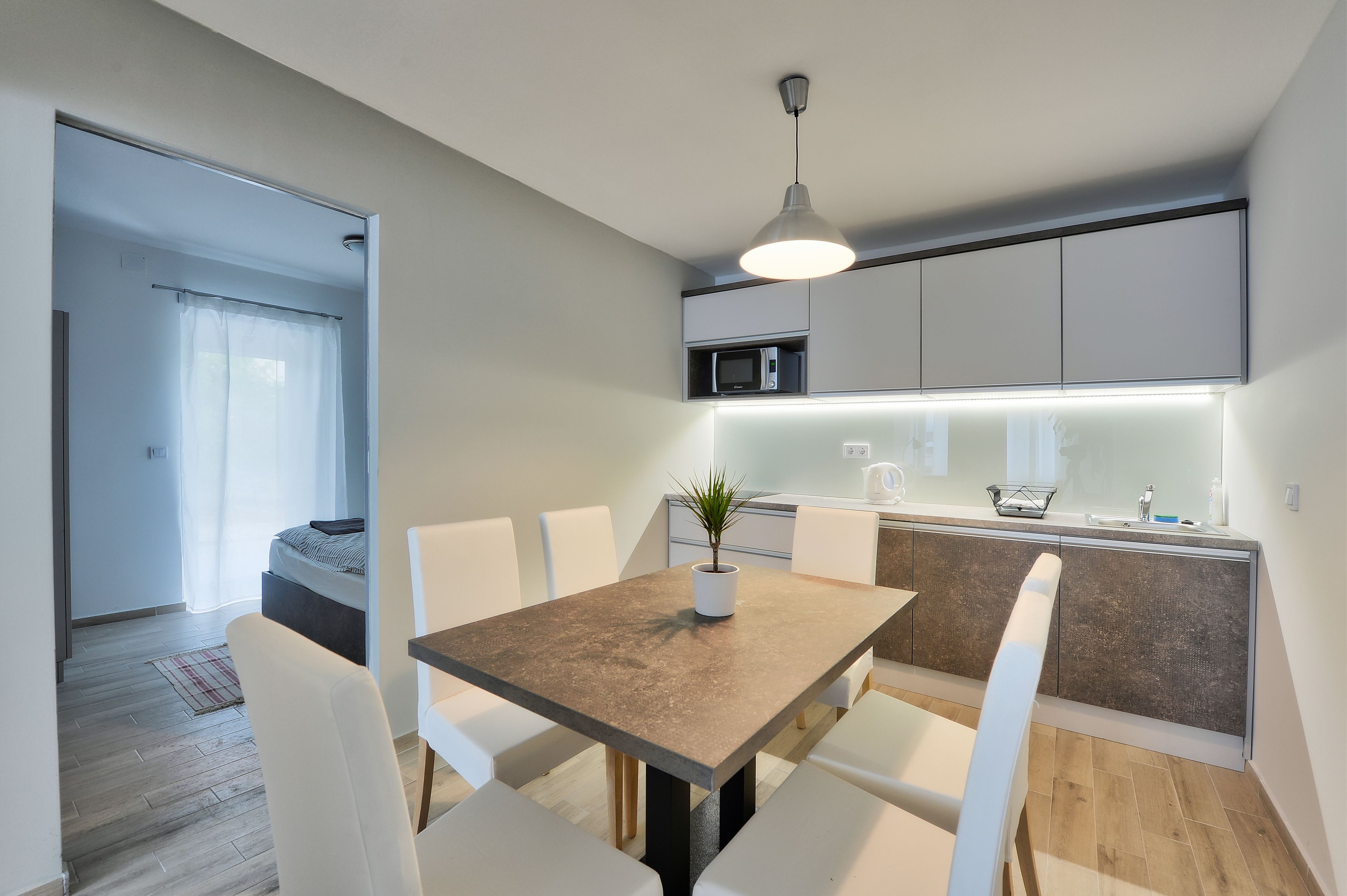 A modern kitchen with a central island, white chairs, a dining table, and a pendant light.