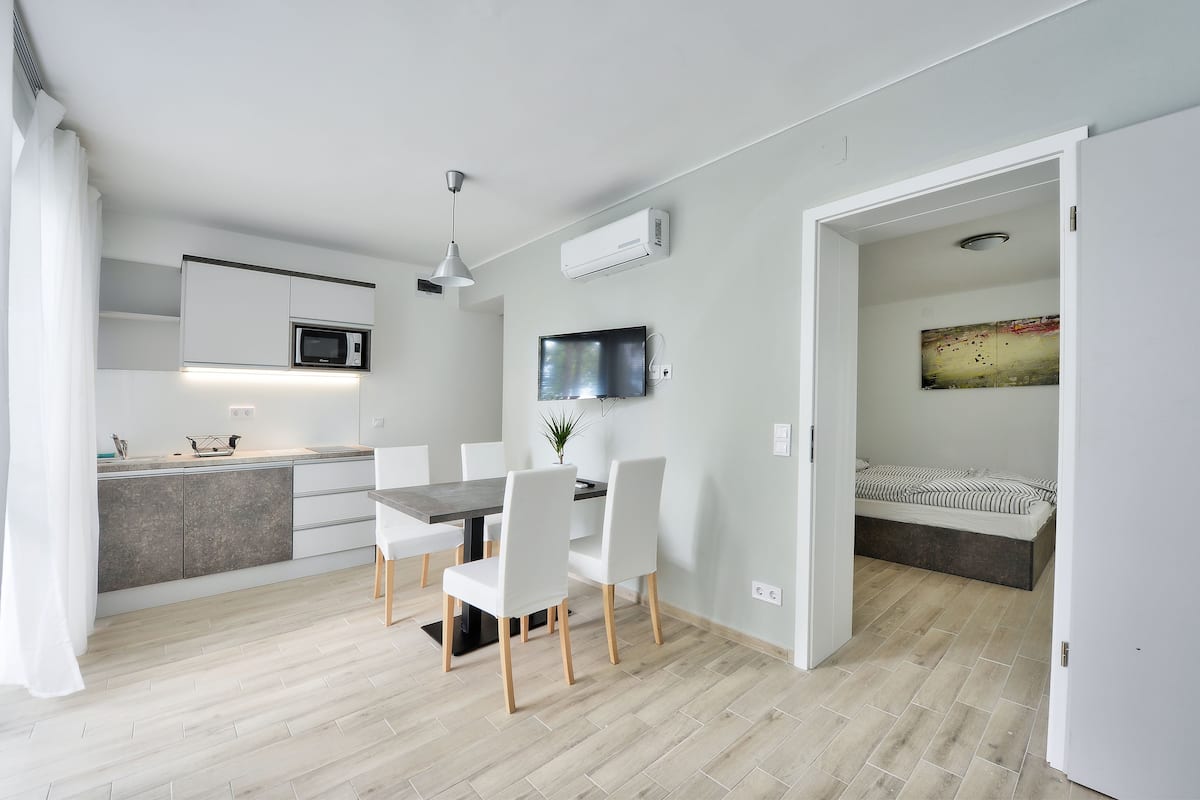 A modern kitchen with white cabinets, a microwave, and a dining area with a table and chairs.