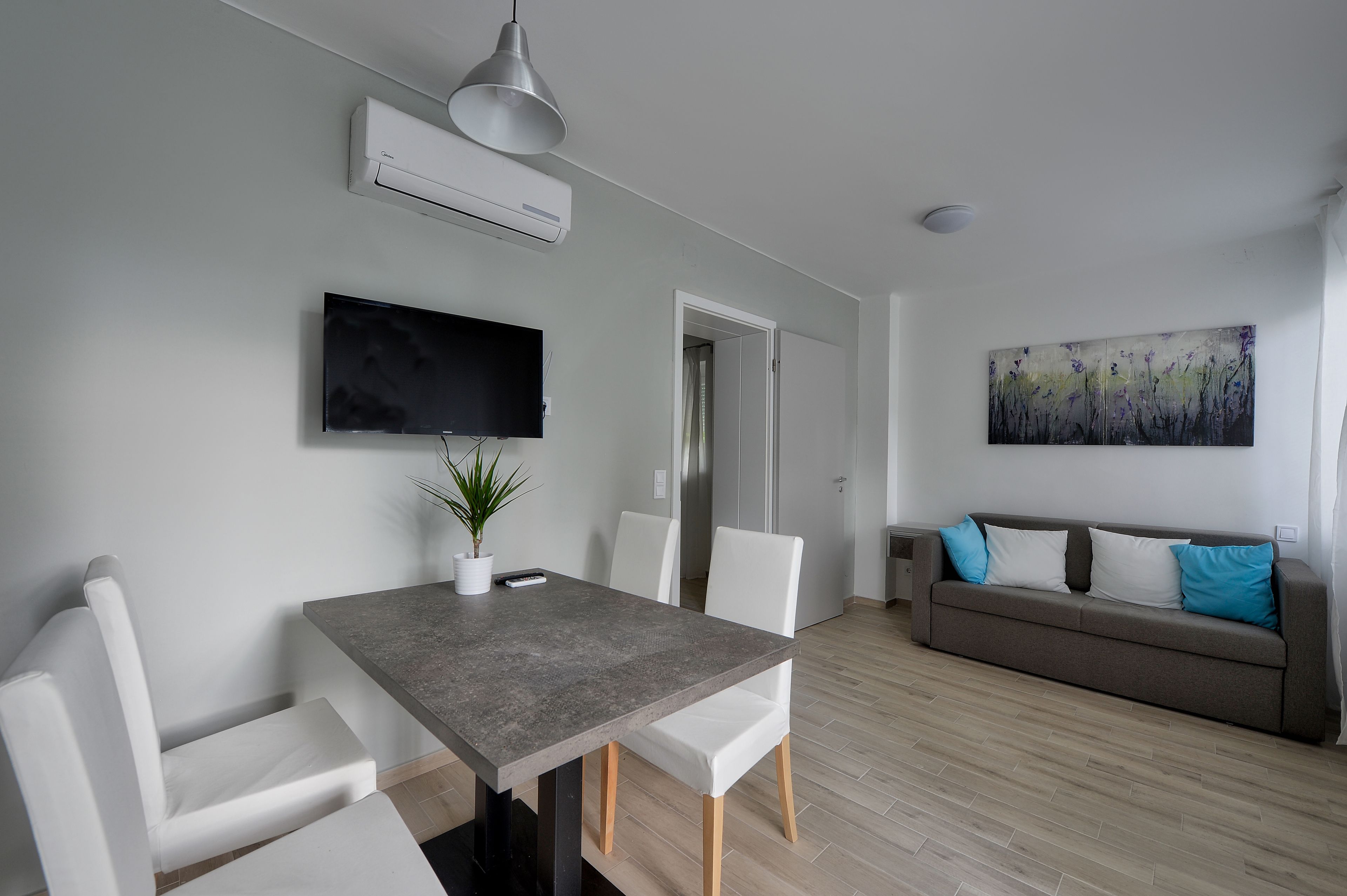 A modern living room with a dining area, a flat-screen TV, a painting, and a sofa with cushions.