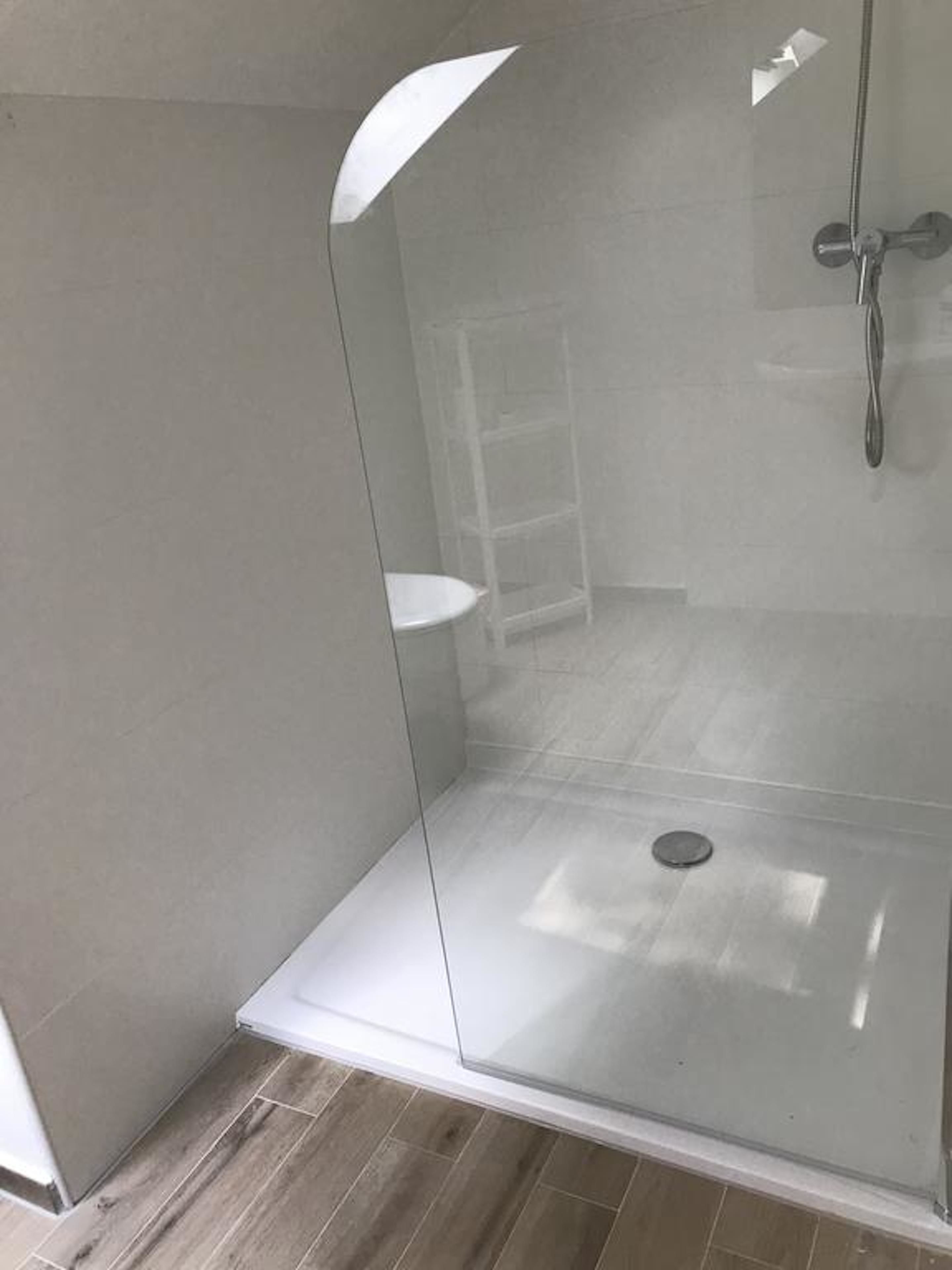 A glass-enclosed shower area with a white sink and a shelf.