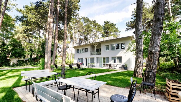 A modern building with a patio area featuring tables and chairs, surrounded by trees. - Villa Oliver 2 Siófok (Siófok)