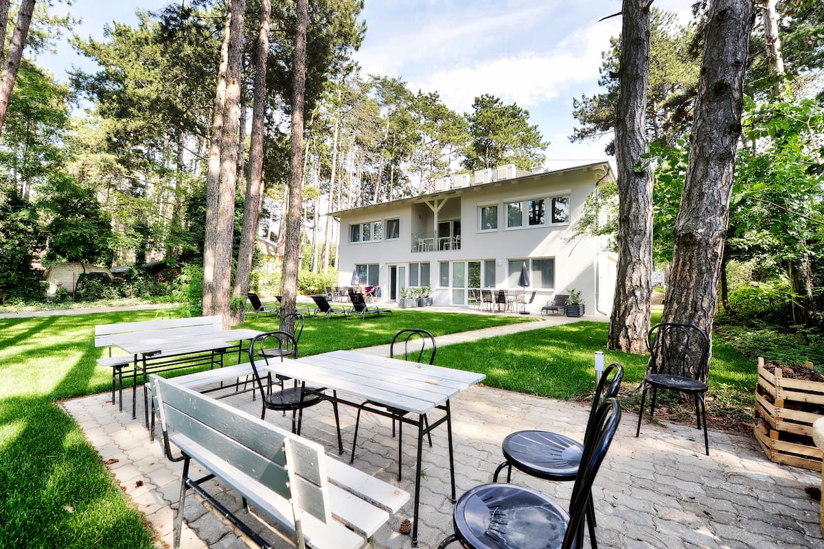 A modern building with a patio area featuring tables and chairs, surrounded by trees.