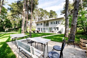 A modern building with a patio area featuring tables and chairs, surrounded by trees. - Villa Oliver 2 Siófok (Siófok)