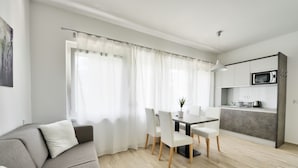A modern living room with a grey sofa, a dining table with chairs, and a kitchen area with a microwave. - Villa Oliver 2 Siófok (Siófok)