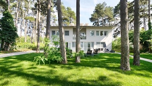 A two-story building with a flat roof, surrounded by tall trees and a well-maintained lawn. - Villa Oliver 2 Siófok (Siófok)