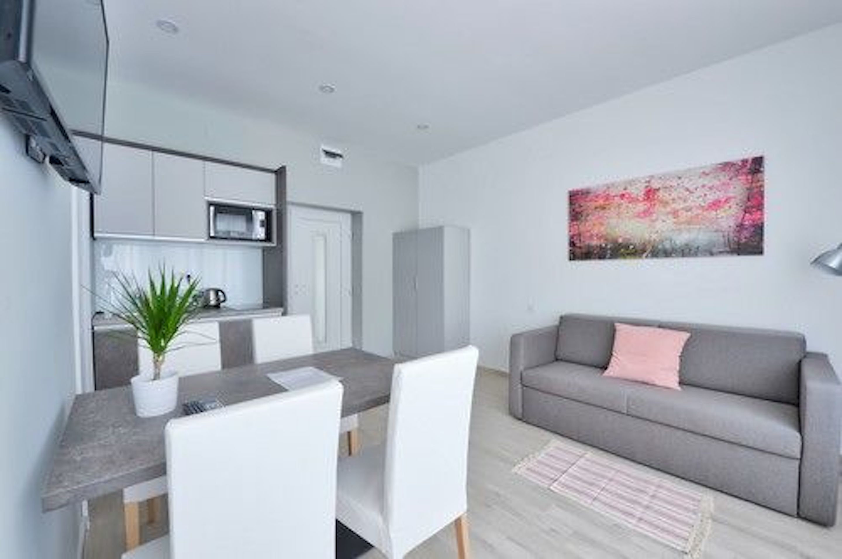 Un salon moderne avec un canapé gris, une table à manger avec des chaises et un coin cuisine équipé de placards et d’un four à micro-ondes.