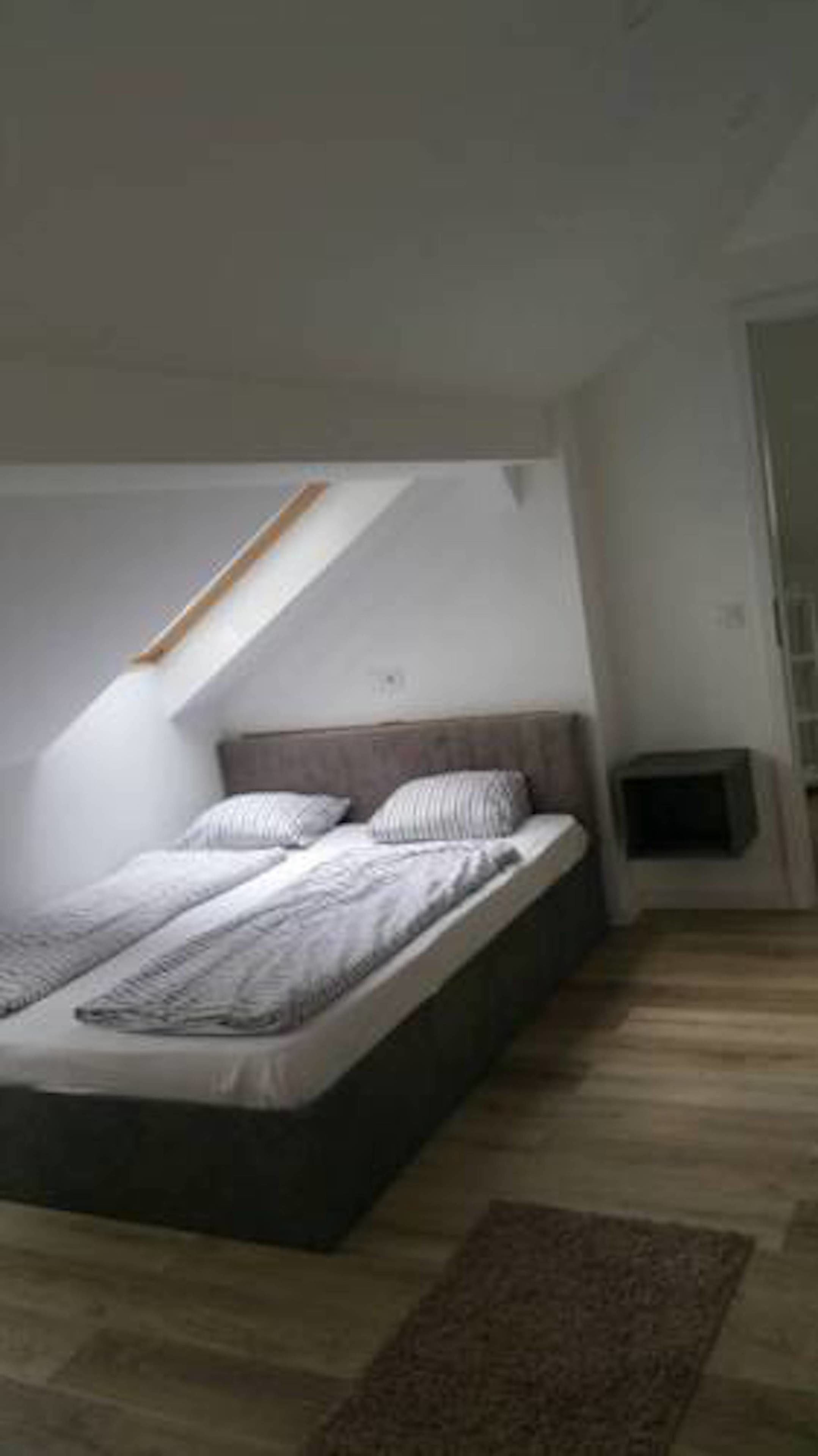A bedroom with a sloped ceiling, a bed with a headboard, and a small television on a stand.
