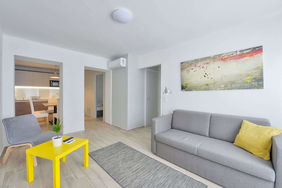 A modern living room with a grey sofa, a yellow coffee table, and a grey rug.