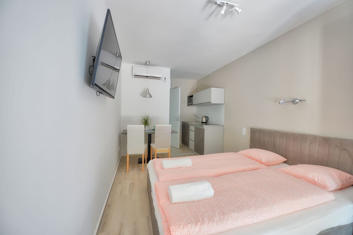 A hotel room with a bed, a desk, a chair, a TV, and a kitchenette.