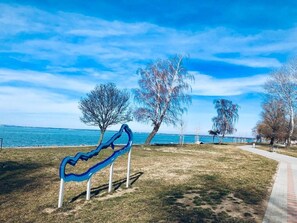 A park with a blue sculpture, trees, and a path by the water. - Villa Oliver 3 Siófok (Siófok)