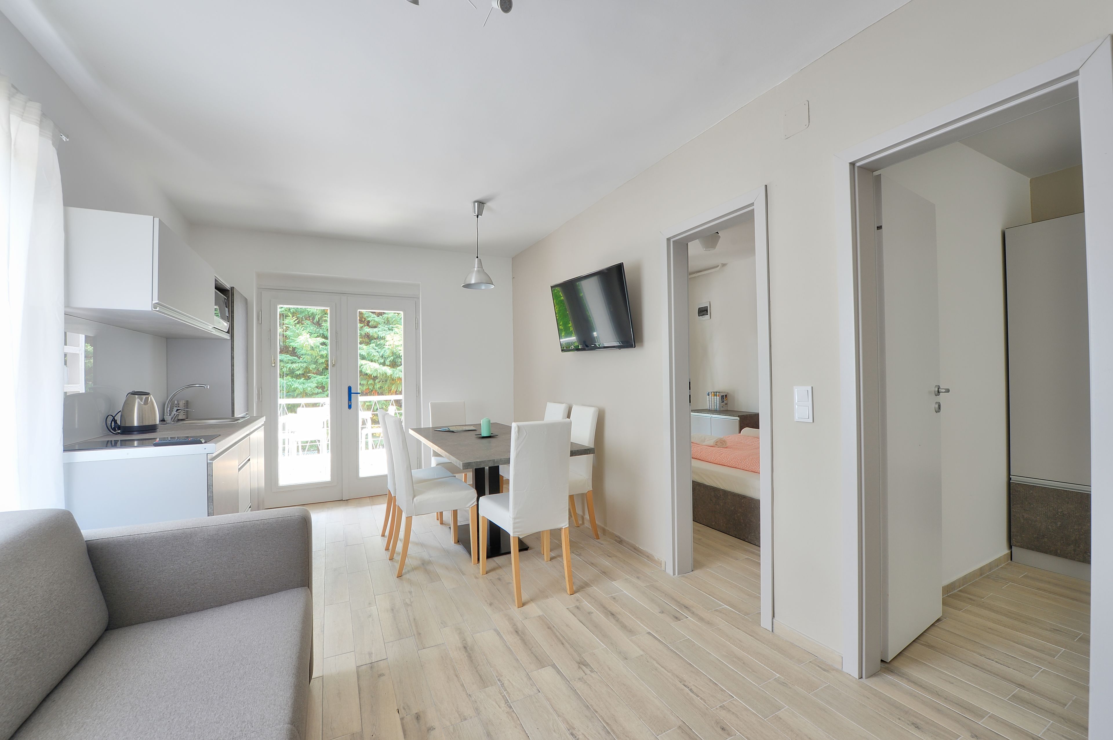 Una sala de estar moderna con sofá, un comedor con mesa y sillas, una cocina con hervidor y un televisor montado en la pared.