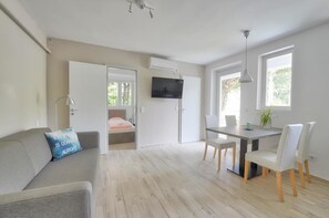 A modern, well-lit room with a sofa, a dining table with chairs, a TV mounted on the wall, and a door leading to another room. - Villa Oliver 3 Siófok (Siófok)