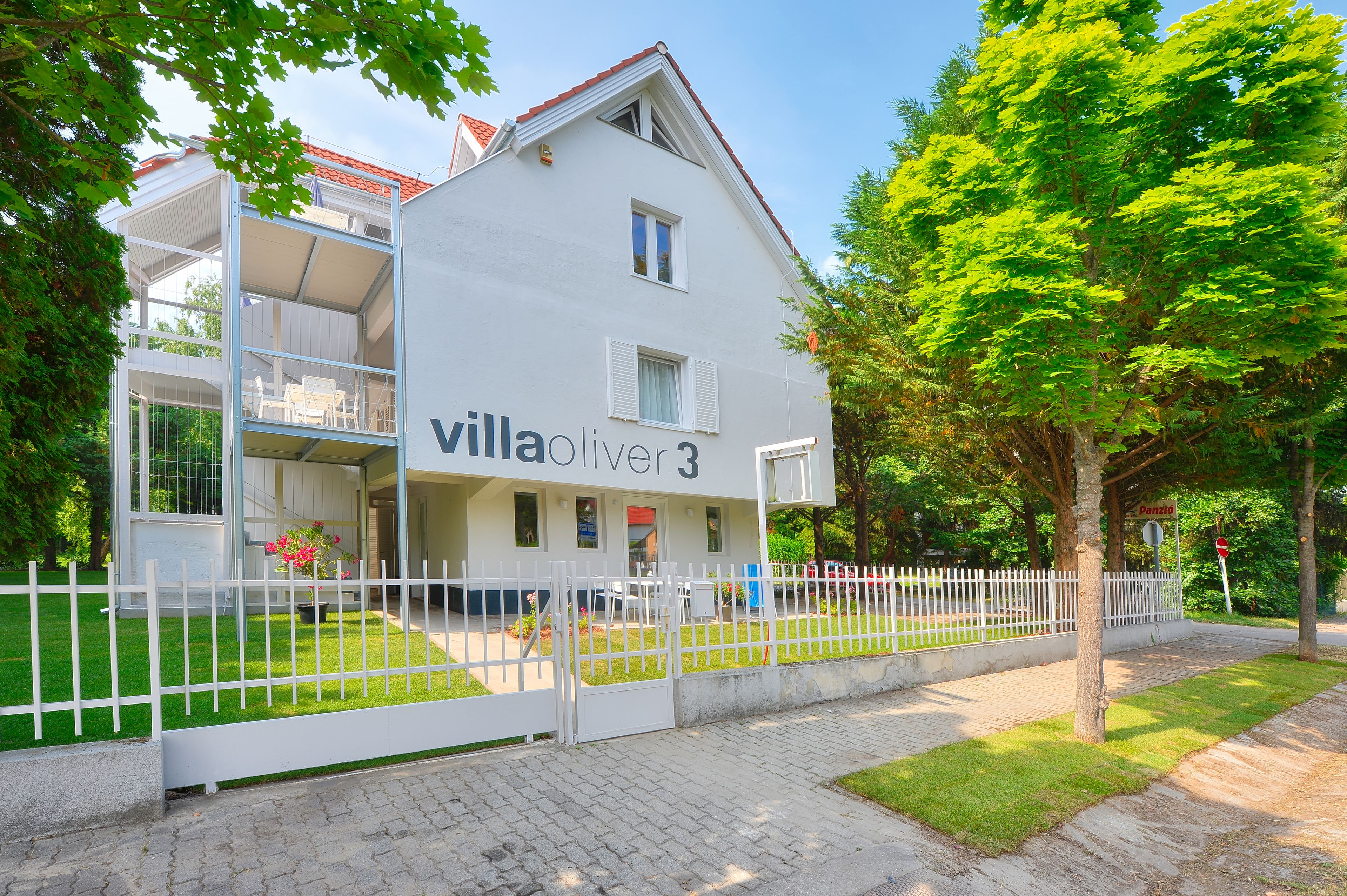 Eine zweistöckige Villa mit Balkon, weißem Zaun und gepflegtem Rasen.