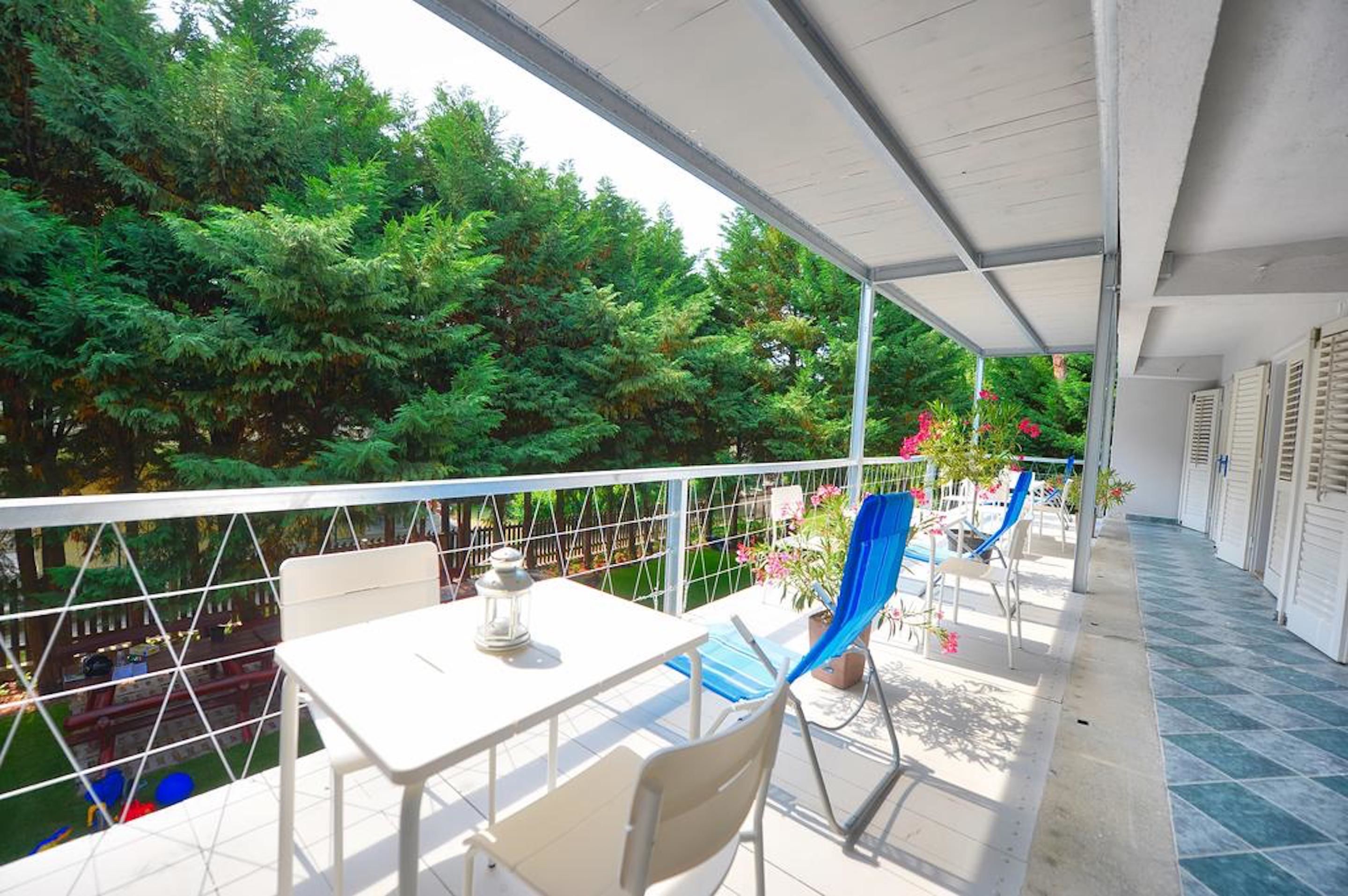 A balcony with a white table and chairs, a railing, and a view of dense green trees.