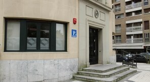 Edifício com placa de estacionamento, alarme de incêndio e porta com degraus que levam à entrada.