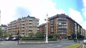 Un immeuble à plusieurs étages doté d’une façade incurvée, un rond-point et un fourgon blanc au premier plan.