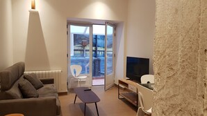 Un salon moderne avec un canapé, une petite table, un téléviseur et un balcon donnant sur l’extérieur.