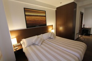 A hotel room with a large bed, a headboard with a mounted picture, a nightstand with a lamp, and a wardrobe. - Pensión Grosen (San Sebastian)