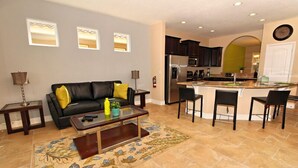 Ein modernes Wohnzimmer mit Sofa, Couchtisch und einer Küchenzeile mit Bar und Sitzgelegenheiten.