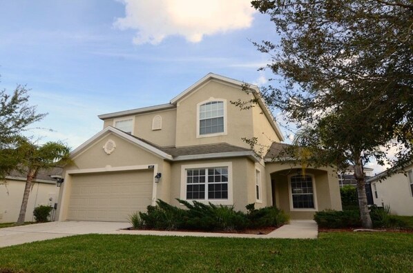 A two-story house with a beige exterior, a garage, and a front yard with landscaping.