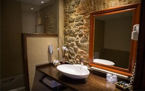 A bathroom with a stone wall, a wooden vanity, a white sink, a mirror, and a hairdryer. - Hotel Casa Beletri (Bejar)
