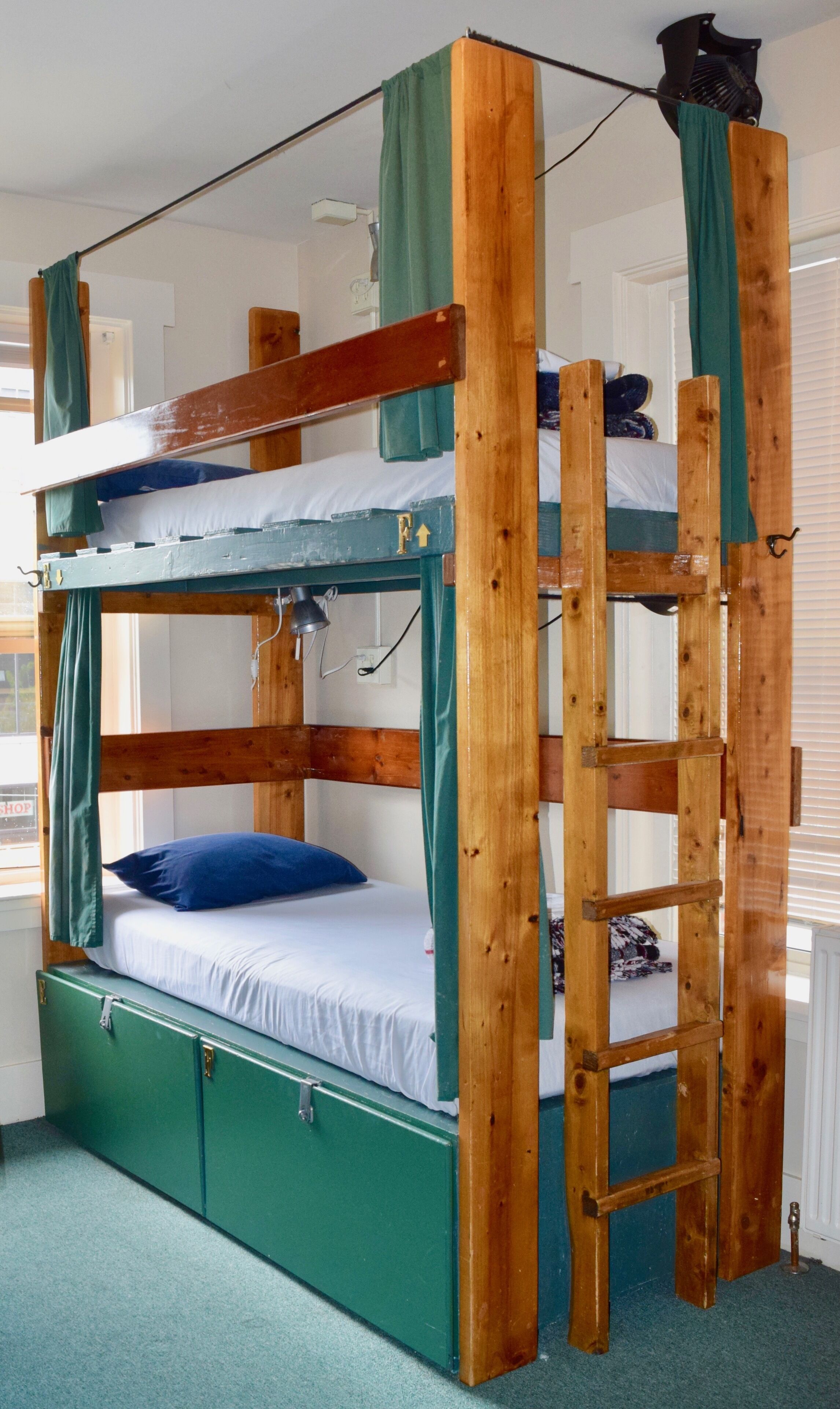 Uma cama beliche com escada, um armário verde e uma janela com persianas.