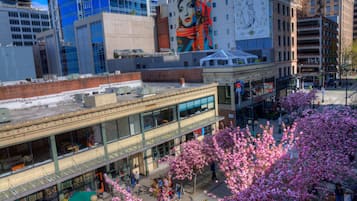 Un immeuble à plusieurs étages doté d’une façade en verre, d’une grande fresque sur le côté et d’une rue bordée de cerisiers en fleurs au premier plan.