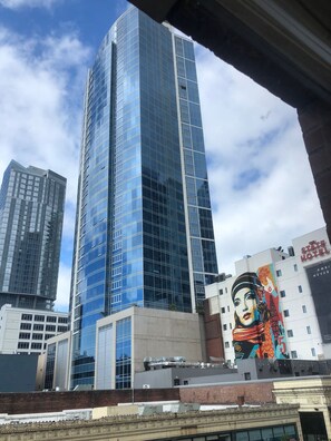 A modern high-rise building with a glass facade, adjacent to a building with a mural and signage for "The State Hotel".