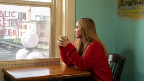 A person sitting at a wooden table by a window with a view of a cityscape and a clock.