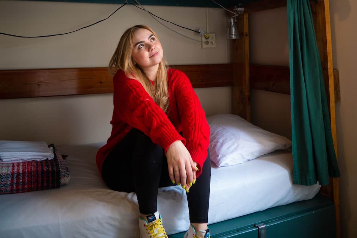 A bunk bed room with a person sitting on the lower bunk and another person standing on the upper bunk.