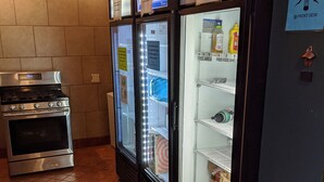 A kitchen with a stainless steel stove, a refrigerator, and a freezer. There are signs indicating a free food shelf area.