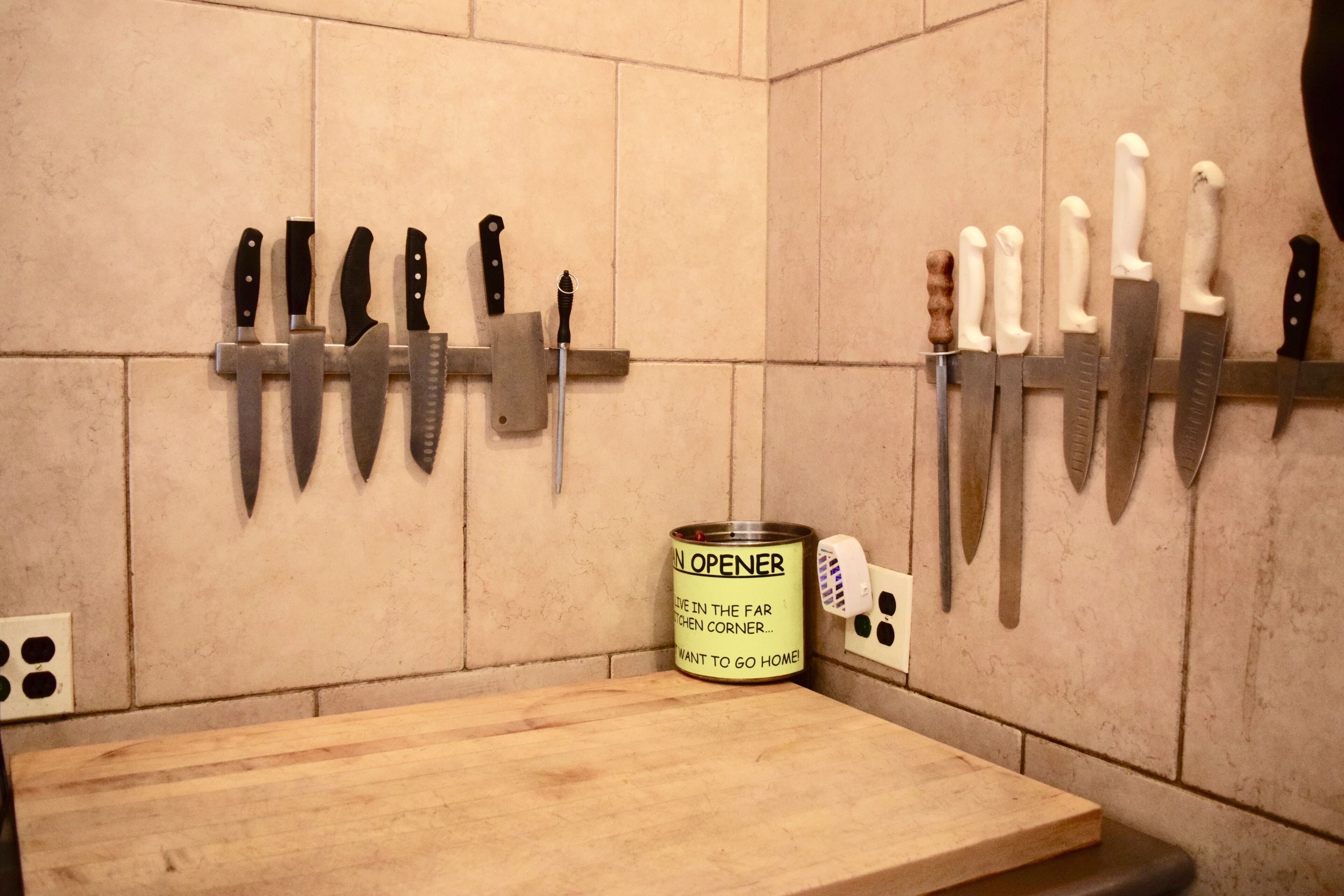 A kitchen with knives mounted on the wall and a can opener on the counter.