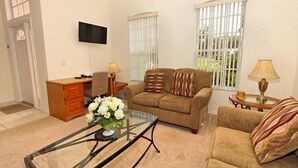 A living room with a sofa, armchair, glass coffee table, and a TV mounted on the wall. - 1842 NHD (Davenport)