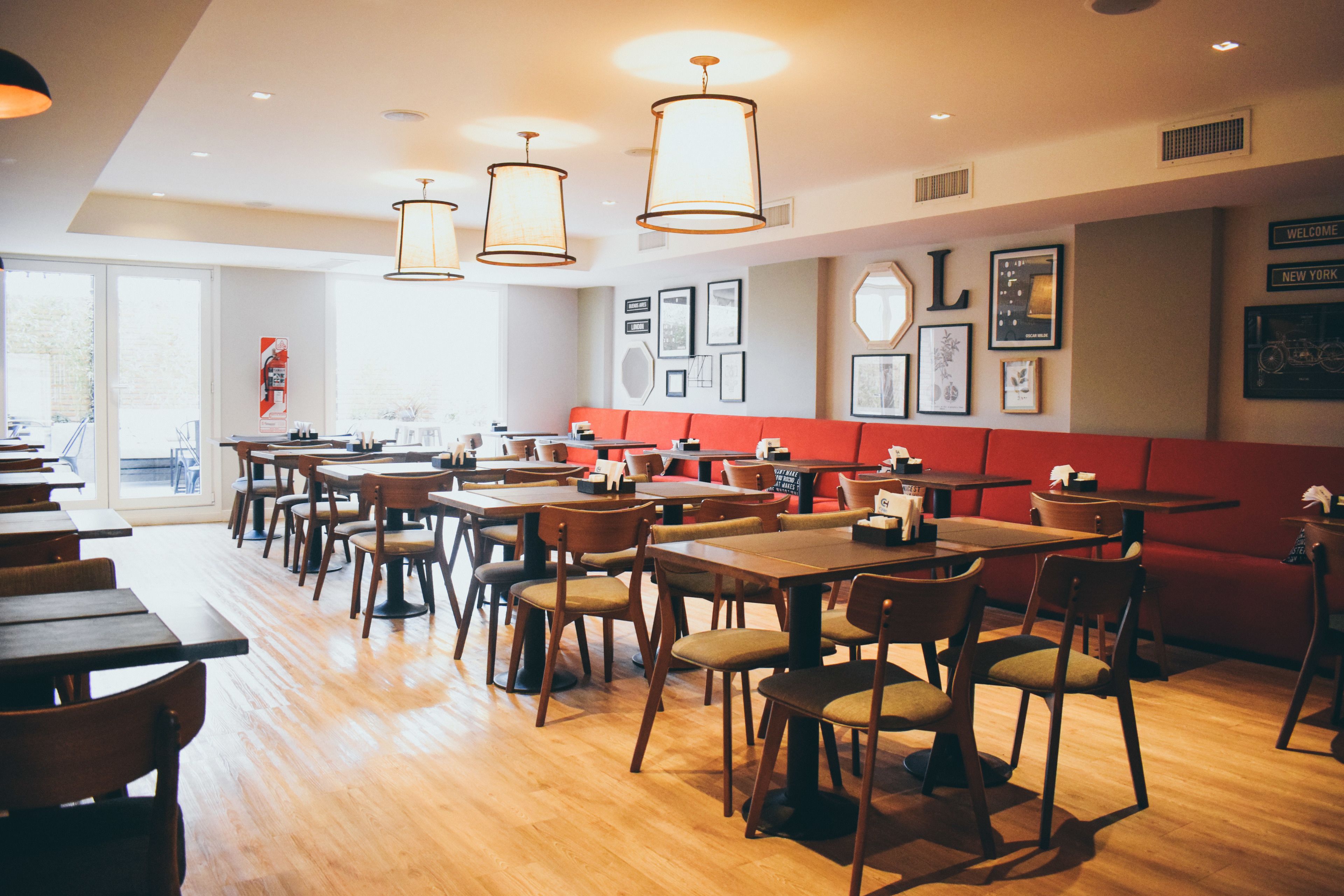A restaurant with wooden tables and chairs, a red booth area, and framed pictures on the walls.