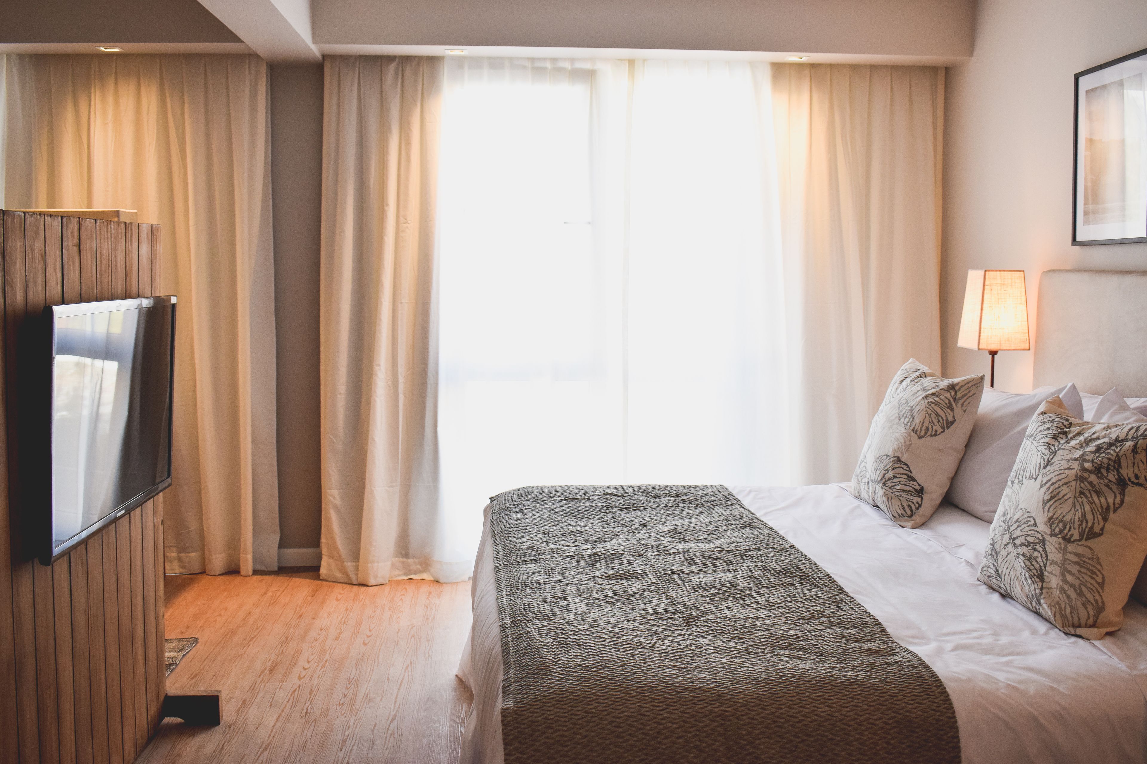 A hotel room with a bed, curtains, a TV, and a lamp.