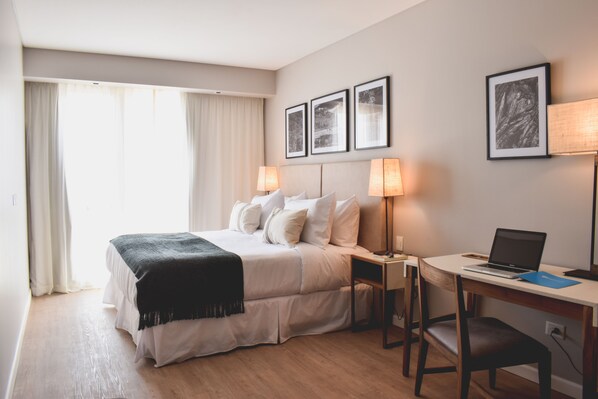 A hotel room with a bed, bedside tables, a desk with a laptop, and framed pictures on the wall. - Cyan Soho Neuquen Hotel (Neuquén)