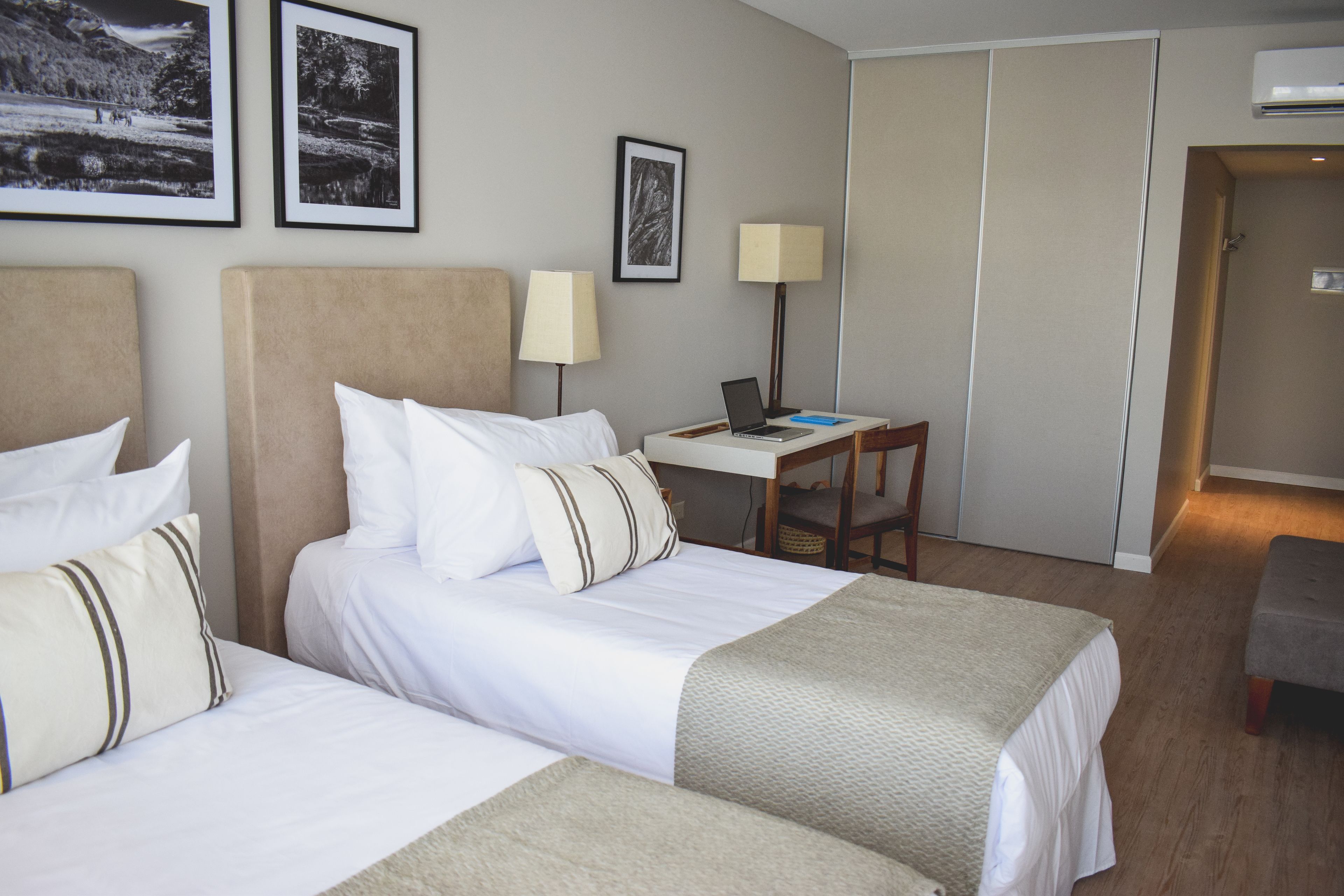Une chambre d’hôtel avec deux lits, un bureau avec un ordinateur portable, une lampe et des tableaux encadrés au mur.